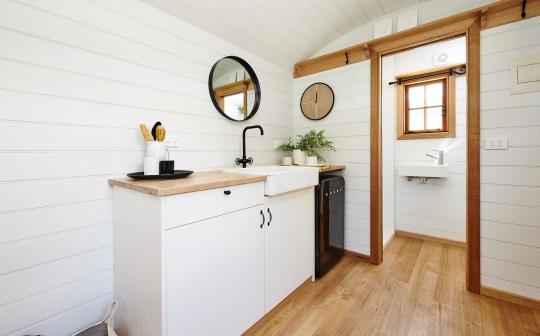 Bright and modern tiny house kitchen with white cabinets and wooden countertops, complemented by natural light