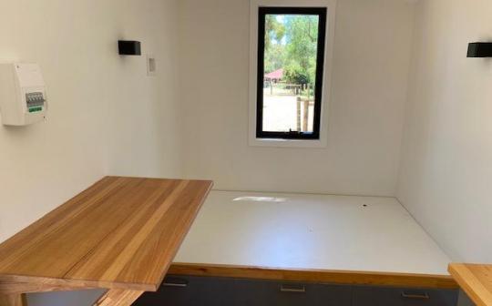 Spacious interior of a tiny house at Eldorado featuring a large bed and a wooden dining table